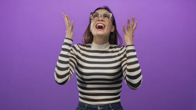 Woman yelling with hands raised and open palms wearing glasses and striped turtleneck in purple studio; frustration release.