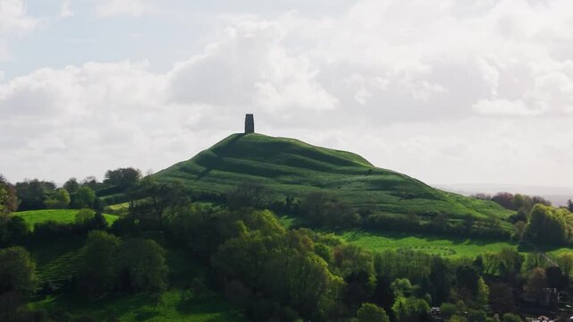 Wide aerial view of Glastonbury Tor rising above the Somerset countryside showing the iconic hill and tower surrounded by green landscape in the United Kingdom