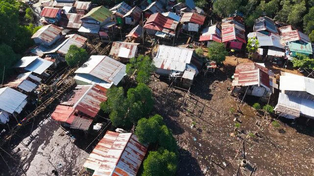 Drone glides above muddy flooded ground with fragile homes and scattered debris