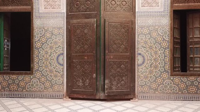 Close view of a traditional Moroccan wooden door surrounded by intricate zellige tile patterns. Rich geometric design and craftsmanship ideal for culture, architecture, and design visuals.