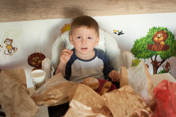 Fototapeta premium A child sits at a table enjoying breakfast. Food wraps and bags are scattered around. The room has animal wall art. The child looks up while holding a piece of food