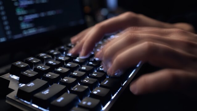 Fast moving hands typing on illuminated mechanical computer keyboard during nighttime.