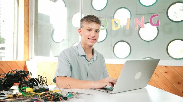 Smart teenager working on laptop and looking at camera at STEM technology class. Caucasian student using computer to analyze data while smiling with confident on table with car model. Edification