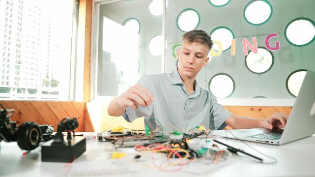 Smart happy boy inspect or learning to use electronic tool to fix car model. high school student studying about electric equipment to repair robotic machines while sitting at STEM class. Edification