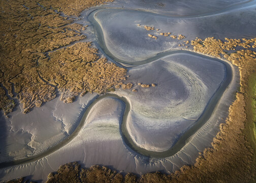 Aerial view of the Rogerstown Estuary featuring winding water channels, textured mudflats, and golden salt marshes at sunset in Lusk, County Dublin, Ireland.