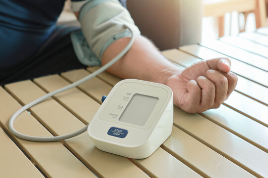 Unrecognizable man measuring blood pressure with digital sphygmomanometer at home. Close up of arm and automatic monitor on table. Healthcare, hypertension awareness and medical self care concept.
