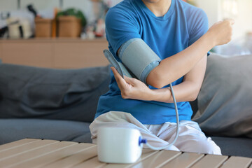 Unrecognizable person applying blood pressure cuff on arm for measuring with automatic digital monitor at home. Cardiology healthcare, monitoring hypertension and daily wellness medical concept.