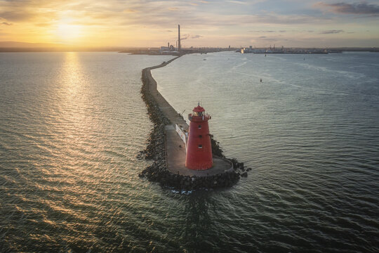 Aerial view of the red Poolbeg Lighthouse at the end of the Great South Wall pier during a golden sunset over Dublin Bay, Dublin, County Dublin, Ireland.