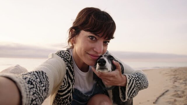 Woman taking a selfie with her dog on the beach at sunrise. Close up shot with natural light, capturing a candid lifestyle moment and connection with pet