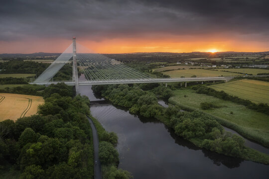 Aerial view of Mary McAleese Boyne Valley Bridge spanning the River Boyne amidst lush green fields and trees at sunset Drogheda, County Louth, Ireland.