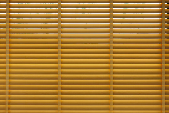 Warm golden sunlight passes through horizontal window blinds, forming repeating lines and soft shadows across a textured surface, illustrating privacy, calm atmosphere, and modern interior design.