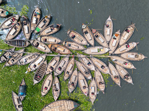 Aerial view of numerous wooden boats clustered on the Buriganga River with green water hyacinths and people in Dhaka, Dhaka Division, Bangladesh.