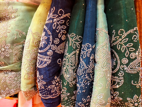 a variety of decorative, embellished fabrics, likely shawls or saris, featuring intricate rhinestone or bead detailing.