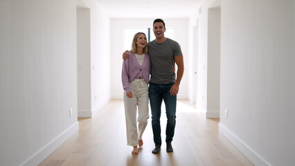 Fototapeta premium Happy young couple walking down empty hallway of their new home. Joyful man and woman moving into unfurnished house
