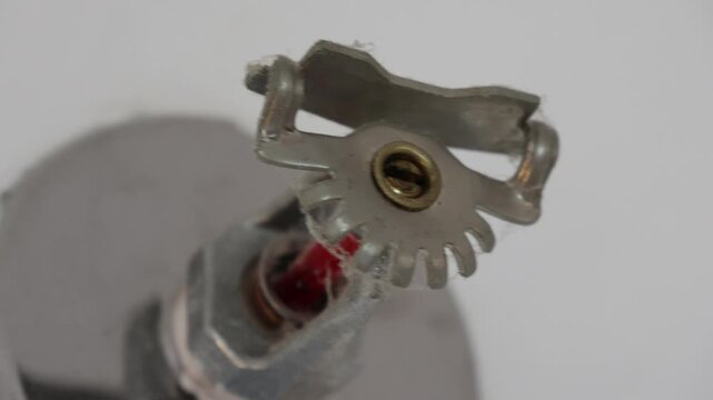 Fire sprinkler head mounted on white ceiling. Metallic finish with red activation component. Securely fastened with visible mounting plate. Ideal for fire safety, building inspection
