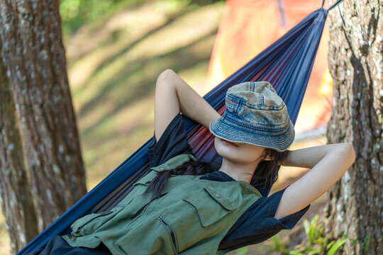 Asian woman resting on hammock with hat covering eyes in forest