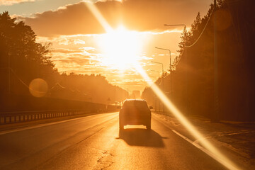 Car moving along an open highway during a vibrant golden hour, with the sun low on the horizon creating warm light and lens flare, evoking concepts of travel, freedom, and an epic road trip © iloli