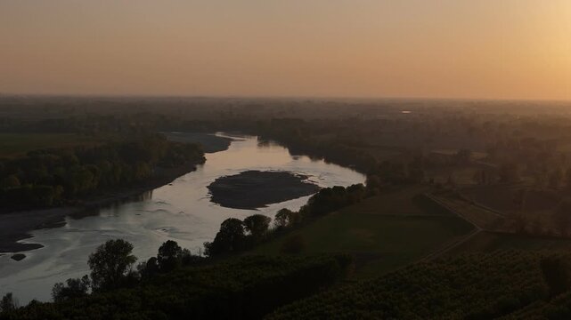 Po River near Spinadesco Cremona at Lombardy Emilia Romagna border with meandering channel and sediment bars across agricultural Po Valley landscape at sunset light, low haze atmosphere, aerial shot