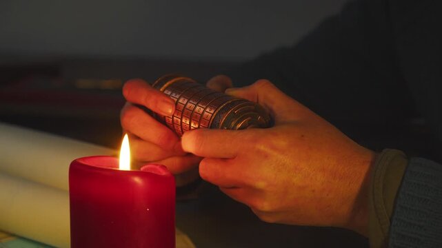 Close-up of glowing candle with shadowed hands working on a cryptex, creating tension and secrecy in a dark, cinematic environment.