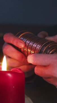 Moody vertical macro of hands attempting to solve a cryptex by candlelight, evoking secrecy, tension, and investigative storytelling.