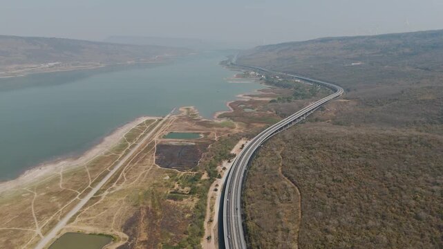 Aerial view of highway running along river and green hills. Transportation, infrastructure, travel and logistics concept