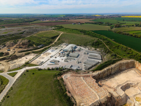 Aerial view of Marshalls Maltby industrial site featuring quarry pits, concrete block storage yards, and surrounding green fields under a clear blue sky in Maltby, England, United Kingdom.