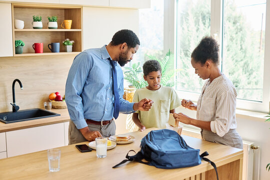 Father businessman mother and father helping son to get ready for school,   helping him with backpack and books, and making snack sandwich in the kitchen  leaving home