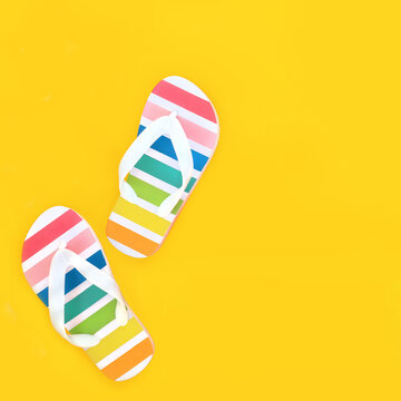 Rainbow flip flops for holiday travel footwear on yellow background. Summer holiday casual fun fashionable rubber striped design.