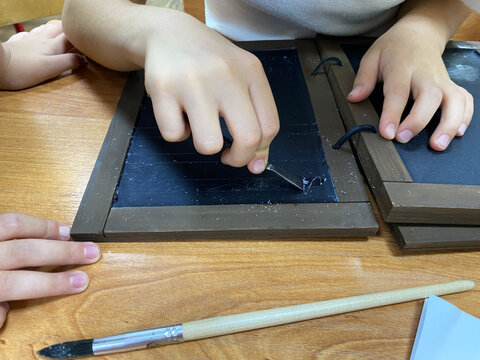 Girl erases an inscription on wax book with metal stylus paddle. Cera (tabula cerata). Analogue of medieval book. Modern replica. Writing with stylus in wax tablets. Study of history