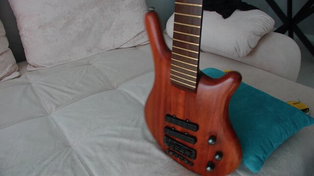 A close-up shot showing a person carefully wiping the natural wood finish of a bass guitar with a pink microfiber cloth. The strings are removed for deep cleaning and maintenance of the instrument's b