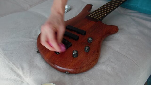 A close-up shot showing a person carefully wiping the natural wood finish of a bass guitar with a pink microfiber cloth. The strings are removed for deep cleaning and maintenance of the instrument's b