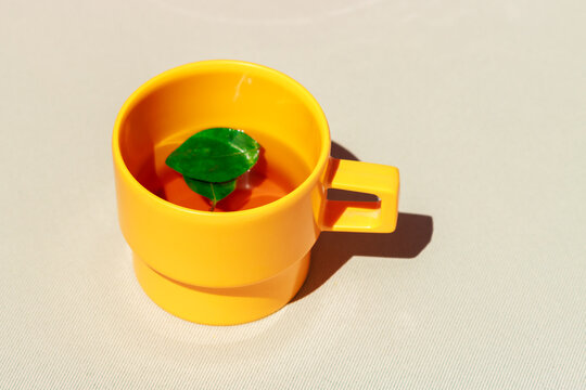 Yellow cup of tea with a green leaf and strong shadow