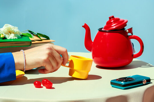 Hand holding a yellow cup with red teapot in colorful still life