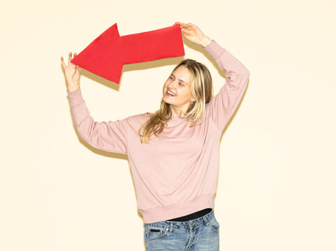 Smiling model holding red paper arrow showing direction and strategy