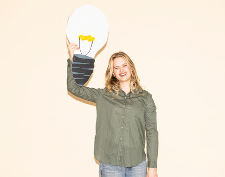 Woman holding a paper lightbulb indoors to show a creative idea