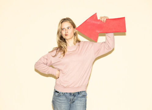 Woman holding large red paper arrow pointing sideways indoors