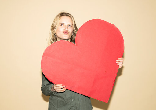 Woman playfully holding a large red paper heart to express love