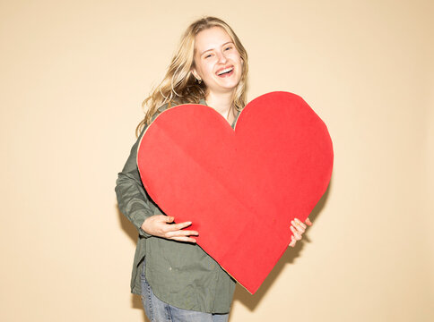 Smiling model holding a red paper heart showing love and empathy