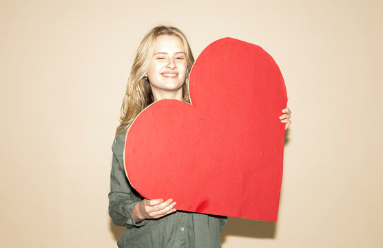 Winking model in green shirt holding a red paper heart