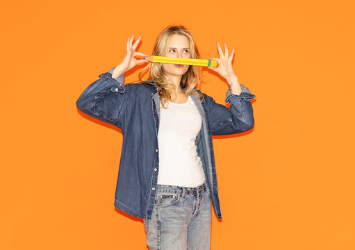 Female student playfully holding paper pencil on orange background