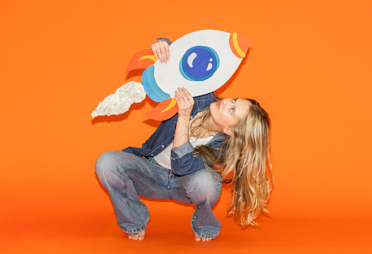 Woman squatting in jeans holding a paper rocket for ambition and success