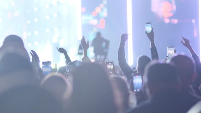 Back view of crowd dancing and clapping on concert dance floor. People jumping raising hands in rhythm. Night music festival atmosphere electronic music event entertainment concept