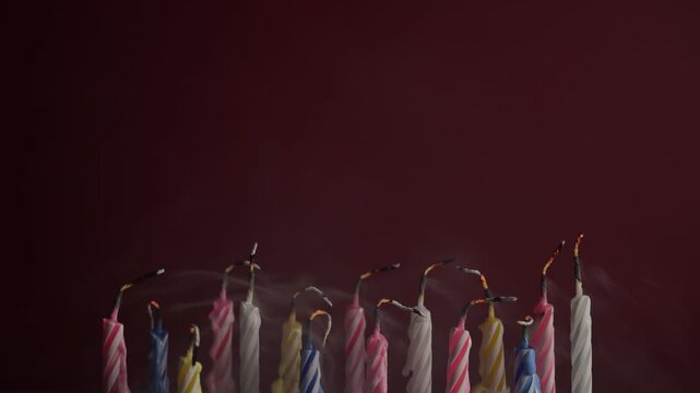 Colorful birthday candles being blown out on red background. Soft smoke rises as flames go out, capturing celebratory and intimate party atmosphere.