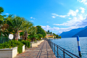 Naklejka premium Von Palmen gesäumte Uferpromenade in Riva di Solto am Iseosee mit Blick auf die Berge, Italien