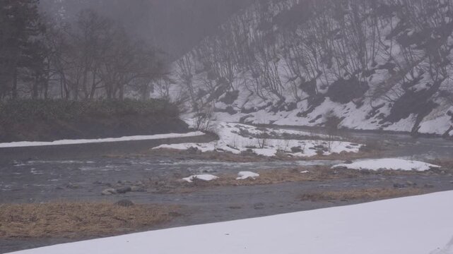 福島県南会津町の伊南川、雪が降る残雪の川岸と冬の山林を流れる清流4K映像
