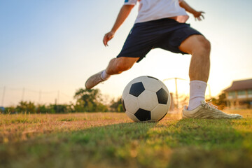 Fototapeta premium Close up of a soccer player kicking a football on a green grass field at sunset