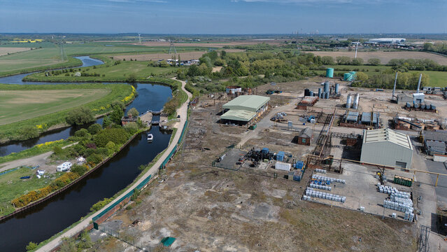 Aerial view of industrial facilities and storage tanks situated alongside a winding canal and lock system under a clear blue sky Knottingley, England, United Kingdom.