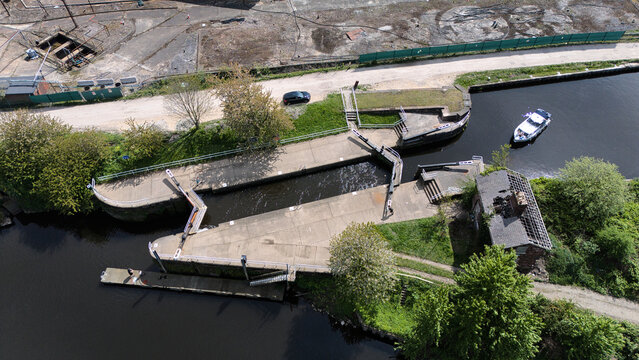 Aerial view of the canal lock system with a boat navigating the water, concrete gates, and a derelict building surrounded by trees in Knottingley, England, United Kingdom.