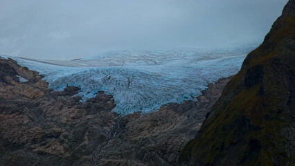 Dramatic glacial landscape, a stunning blue ice glacier nestled between rugged dark mountains, showcasing the raw power of nature and climate change impact © Shanza