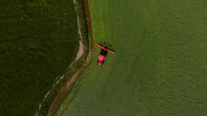 Aerial view of a vibrant green agricultural field, a red tractor cultivating crops, modern farming machinery in action, lush farmland landscape for sustainable agriculture. © Shanza
